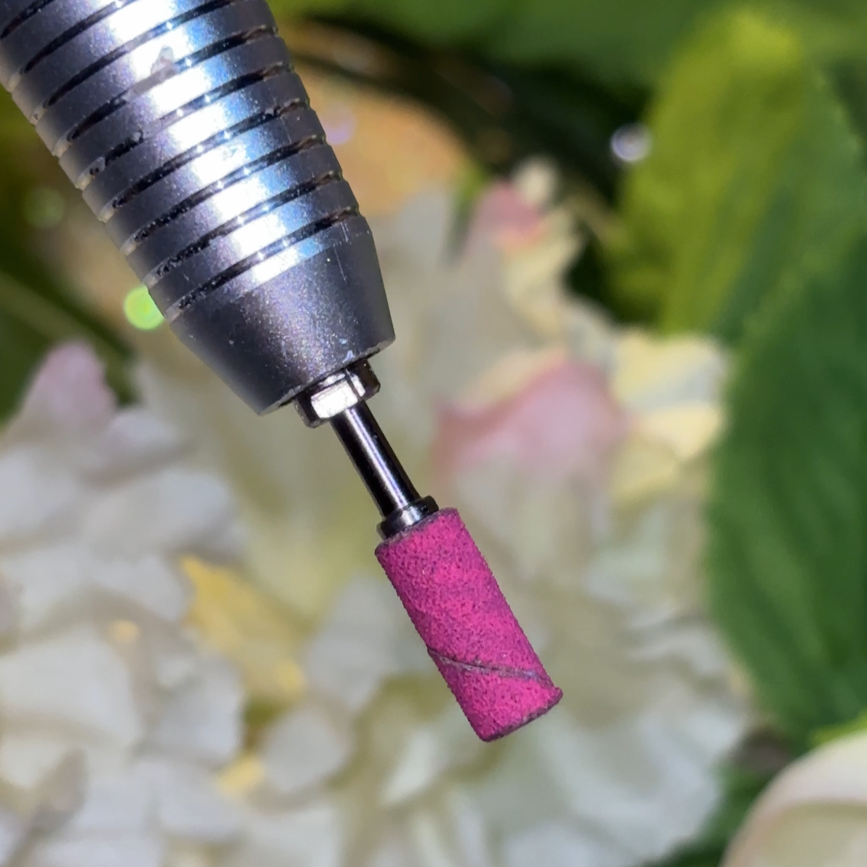 Close-up image of a silver-colored mini mandrel barrel with a pink sanding band , indicating its use for nail care. 3mm sanding band.