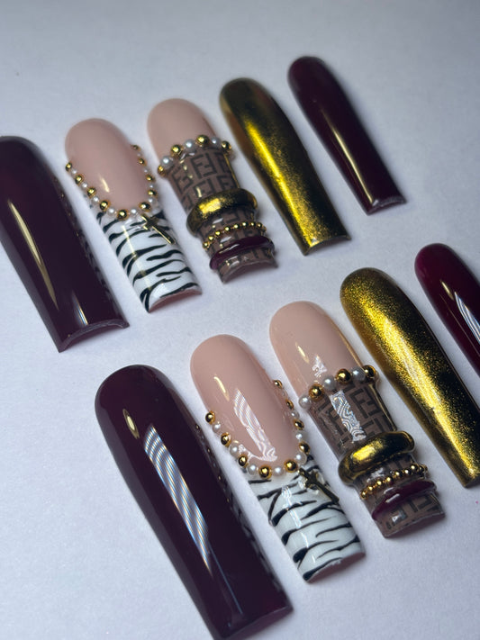 Collection of nail art designs on a white background. Burgundy, Zebra print, and gold nail colors on press-on nails. 15 piece nail set.