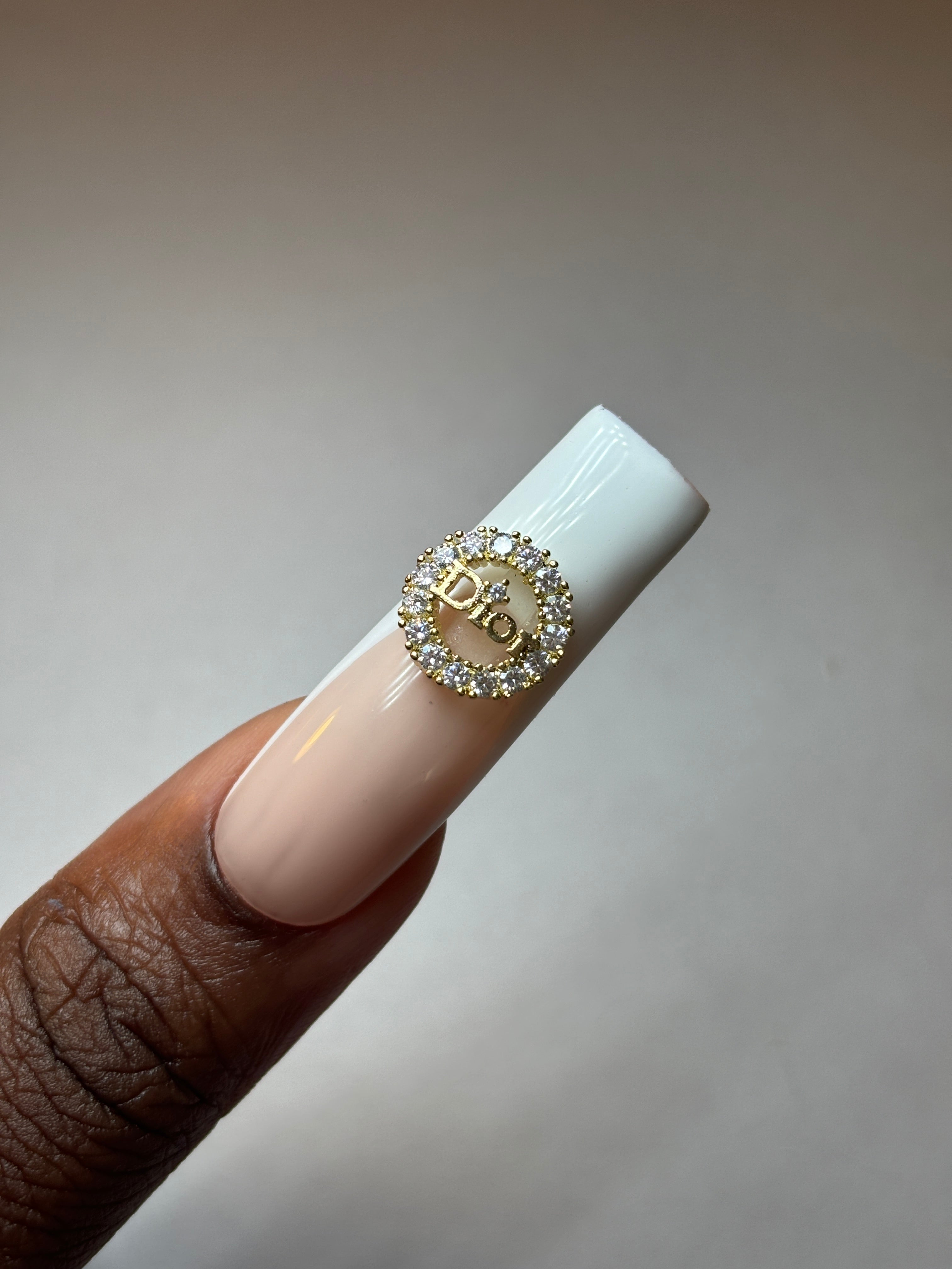 French tip nail with dior diamond studded nail emblem on it. Depicting a nail charm or decoration for nails. 